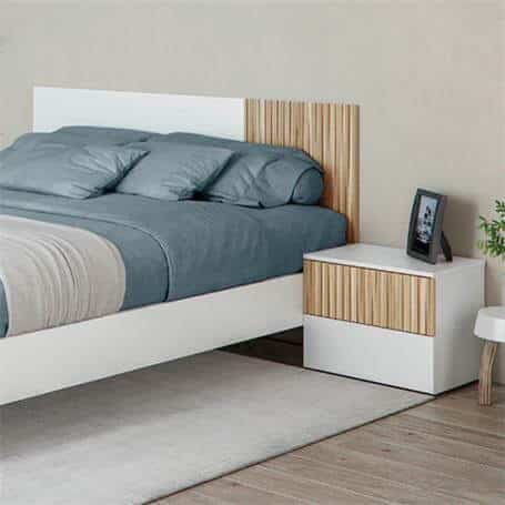 Mesita de noche junto a cama en ambiente decorado con textiles claros y luz natural